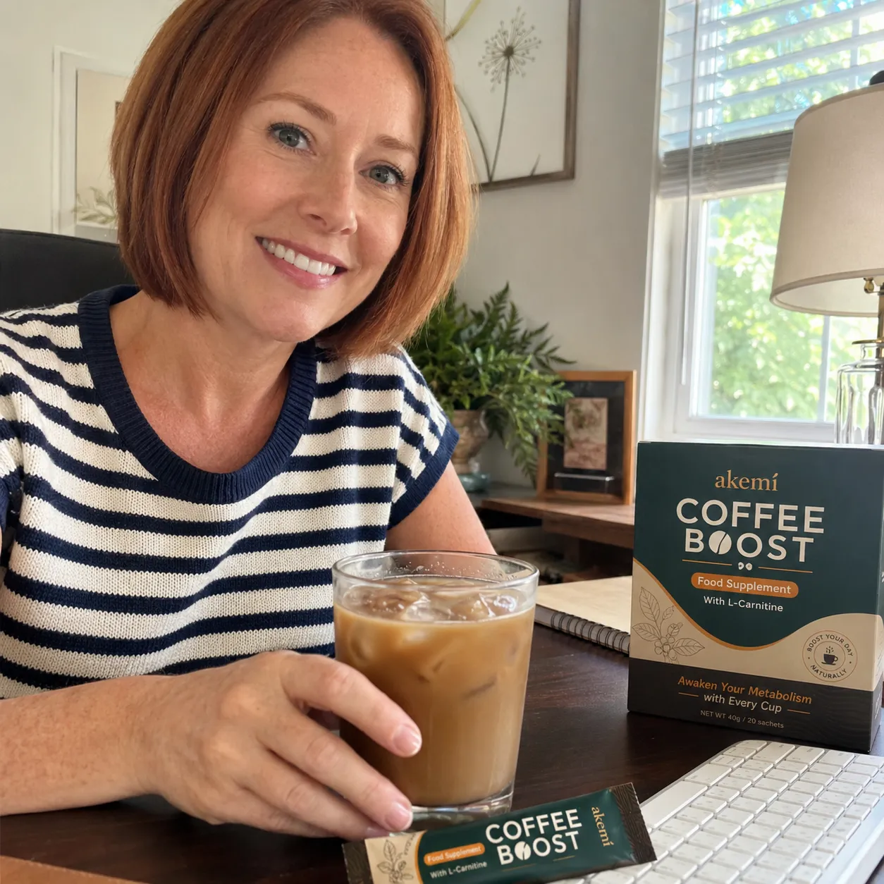 Seller photo: a woman at a desk with iced coffee and Akemi Coffee Boost box and sachet on the table